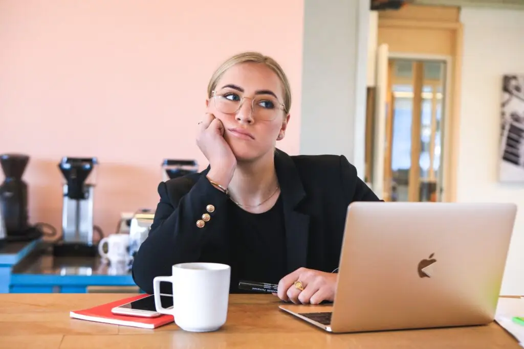 thinking pose of a professional women while holding his pen and facing her laptop in apple unit while looking away