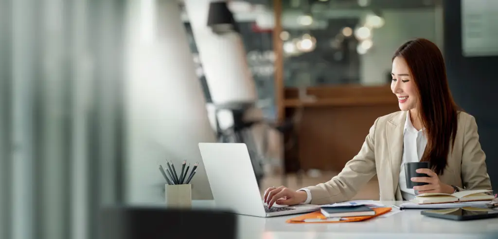 smiling professional checking her laptop while handling cup of coffee in a coffee shop set up