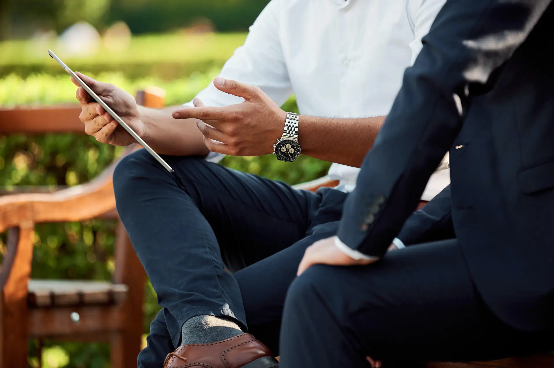 two professional sitting in a bench while one professional is handling a gadget and pointing his finger for presentation