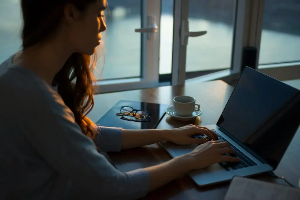 professional women typing to her laptop with a cup of coffee and a reading glass behind