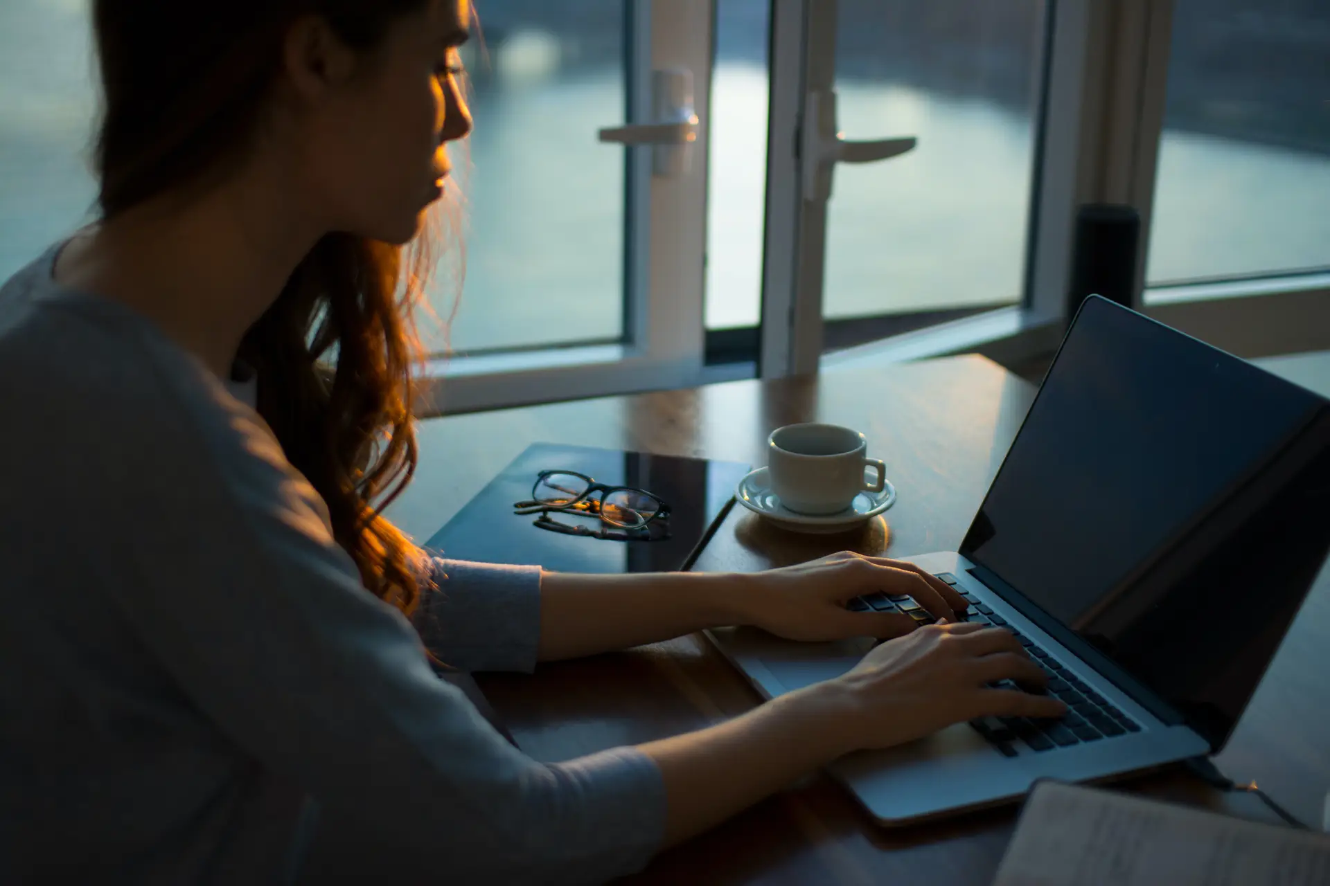 professional women typing to her laptop with a cup of coffee and a reading glass behind