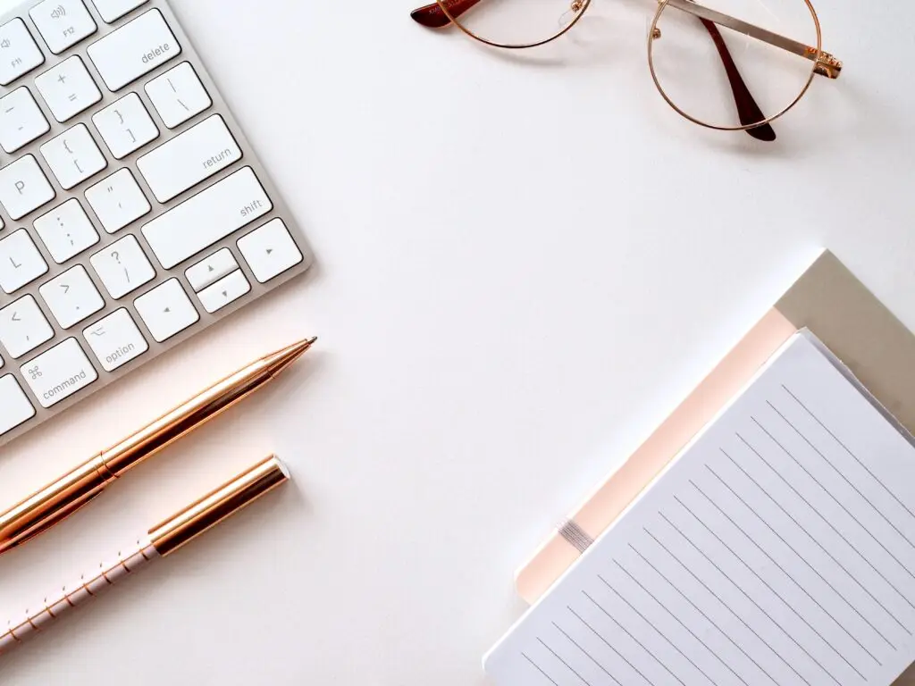a clean desk with reading glass on top keyboard right side and a pen and a note below