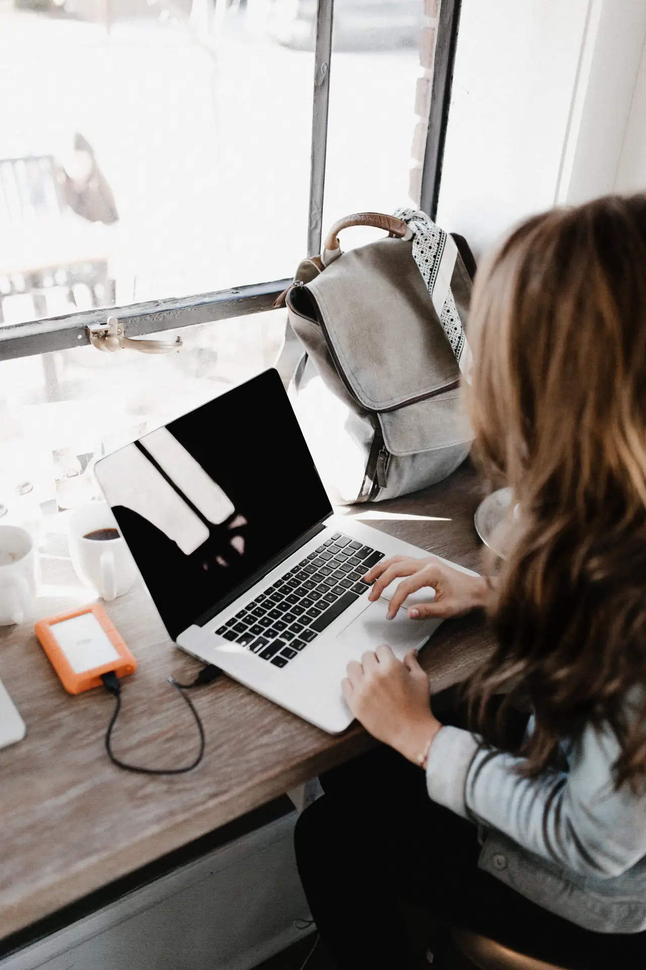 professional women using her laptop with external drive plug in her laptop in a clean desktop with her bag behind