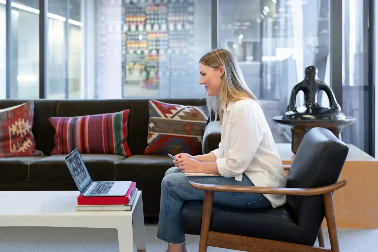 sitting a professional women facing downward her laptop during a virtual meeting in a fancy living room