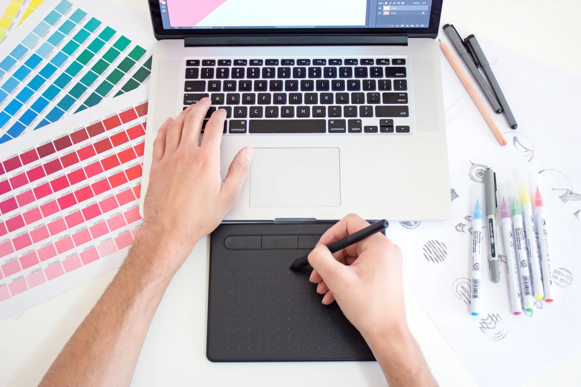 a top view of typing on a laptop while handling a pen for stech with color pallete chart and pen around the laptop